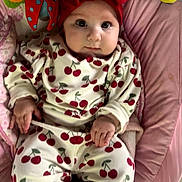 Marlie is registered to the contest to win money with this photo: baby, infant, child, red_bow, cherry_pattern, clothing, pink_cushion, toy, colorful_toy, face, hand, lying_down, cute, wide_eyes, headband, comfort, indoor, portrait, baby_outfit, soft_fabric