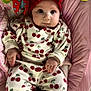 baby, infant, child, red_bow, cherry_pattern, clothing, pink_cushion, toy, colorful_toy, face, hand, lying_down, cute, wide_eyes, headband, comfort, indoor, portrait, baby_outfit, soft_fabric