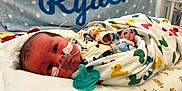 Ryder is registered to the contest to win money with this photo: newborn, baby, infant, blanket, pacifier, nasal_tube, hospital, bed, swaddled, cute, sleeping, child, face, person, medical, healthcare, colorful, pattern, blue, white