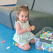 Romy participe au concours pour gagner de l'argent avec cette photo : toddler, child, playing, toys, blocks, colorful, floor, blue_floor, plastic_container, gray_couch, indoor, smiling, happy, girl, shorts, sleeveless_top, hair_bow, kneeling, casual_clothing, daylight