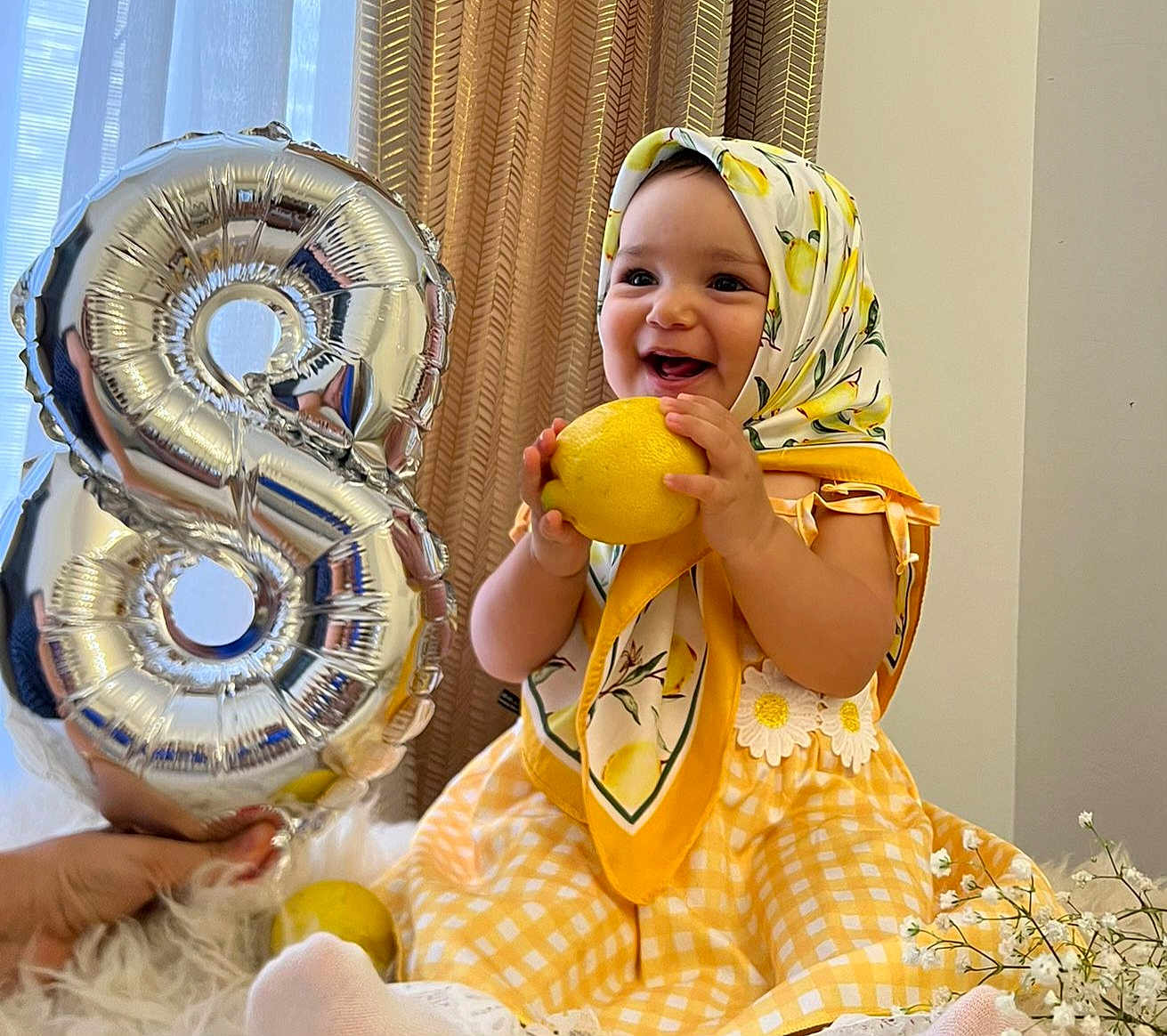 Zina a rejoint le concours — aidez-le/la à gagner de superbes lots ! baby, child, toddler, smiling, yellow_dress, headscarf, lemon, balloon, number_8, curtains, flowers, indoor, happy, celebration, holding, sitting, cute, portrait, bright, decor