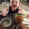 toddler, child, happy, smiling, toy, goblet, hand, table, living_room, carpet, dog, dog_crate, blanket, furniture, person, indoor, playful, expression, home, baby