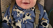 Zane joined the competition — help win amazing prizes! baby, baby_seat, babywear, blue_onesie, child, closeup, clothing, cow_pattern, cute, face, furniture, hand, happy, indoor, infant, portrait, seatbelt, sitting, smiling, young_child