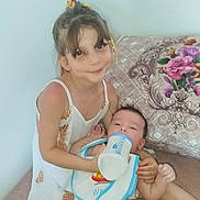 Naïma a rejoint le concours — aidez-le/la à gagner de superbes lots ! baby, bib, bottle, child, couch, cushion, cute, diaper, dress, family, feeding, floral, hair_tie, indoor, love, person, pineapple_pattern, sitting, smile, toddler