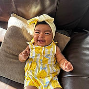 Sierra joined the competition — help win amazing prizes! baby, brown_leather, cheeks, child, clothing, couch, cute, happy, headwrap, indoors, infant, lemon_pattern, pillow, portrait, relaxed, romper, sitting, smiling, sunlight, yellow_clothing