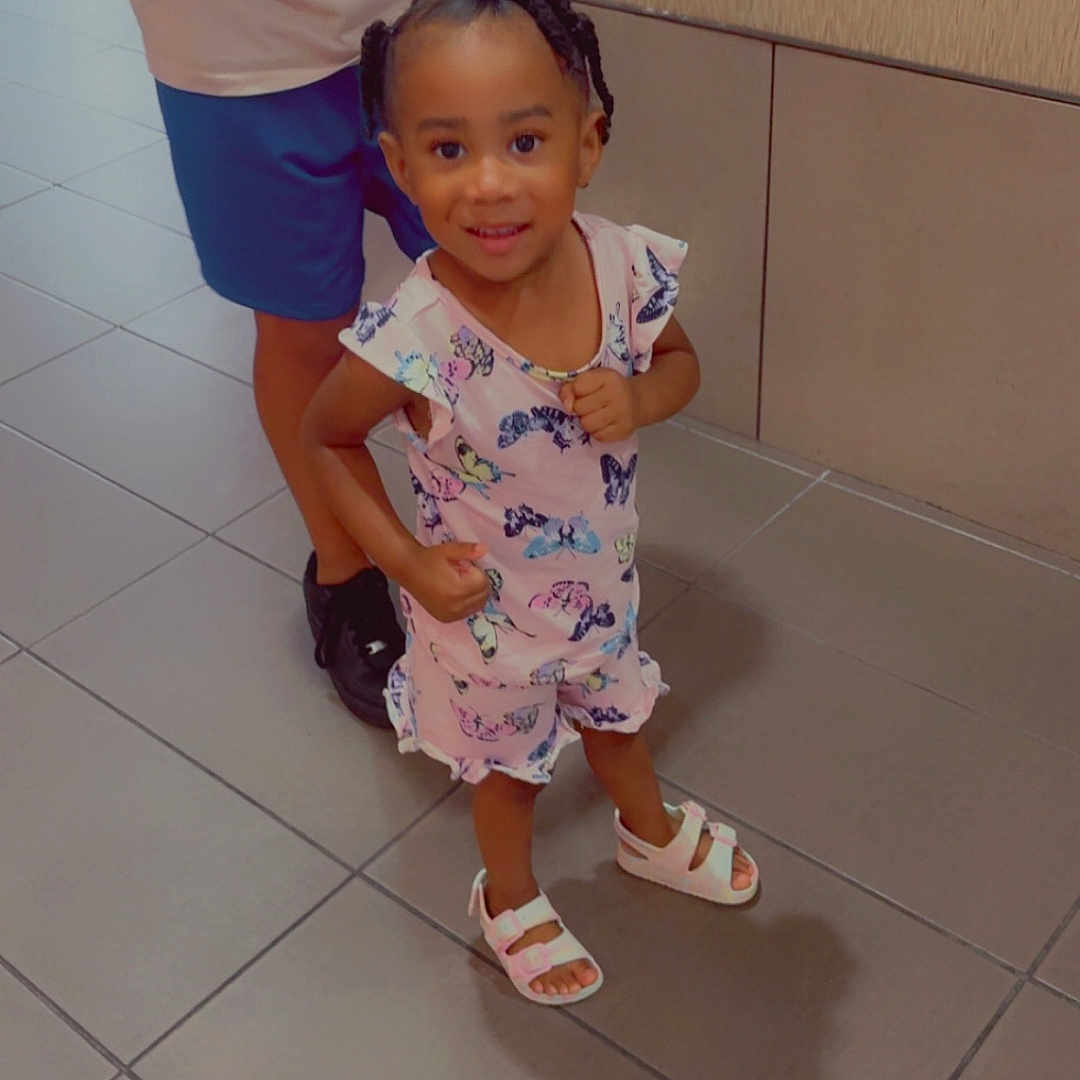 Kaizlynn Mitchell joined the competition — help win amazing prizes! background_wall, braided_hair, butterfly_pattern, casual_clothing, child, feet, floor_tiles, girl, happy, indoor, legs, person, pink_dress, playful, sandals, shadow, smiling, standing, toddler, young_child