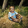 baby, child, smiling, outdoor, grass, trees, denim_overalls, sandals, nature, cute, happy, sitting, infant, sunlight, greenery, playful, young, portrait, toddler, casual_clothing