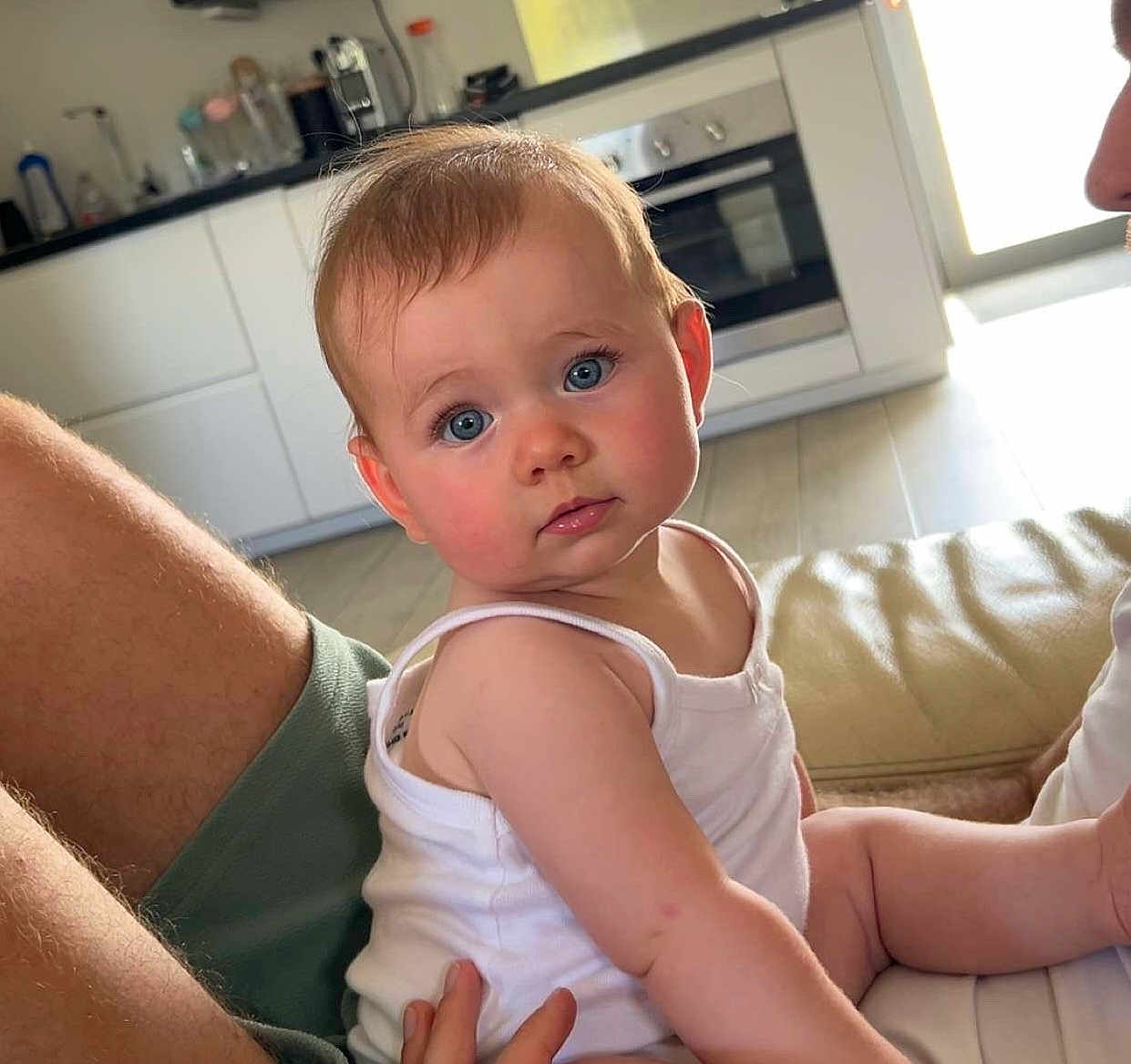 Alba participe au concours pour gagner de l'argent avec cette photo : baby, child, blue_eyes, white_tank_top, curious, indoor, kitchen, couch, person, sitting, skin, arm, face, hair, light, window, floor, home, expression, furniture