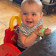Alba a rejoint le concours — aidez-le/la à gagner de superbes lots ! baby, child, high_chair, striped_shirt, blue_eyes, smiling, happy, clapping, sauce_packet, restaurant, table, wooden_table, tile_floor, booth_seating, indoor, person, cute, infant, casual_clothing, seat