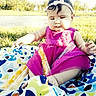 baby, child, outdoor, grass, pond, dress, pink, blanket, food, popsicle, summer, sunlight, headband, curly_hair, sitting, cute, nature, playful, infant, happy