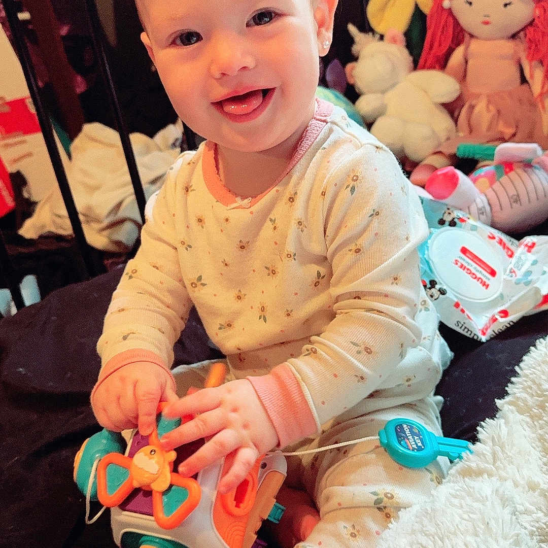 Aurora is registered to the contest to win money with this photo: baby, baby_wipes, bed, blanket, child, cute, face, foot, furniture, hands, happy, indoor, infant, pajamas, playing, plush_doll, room, smiling, toy, unicorn_toy