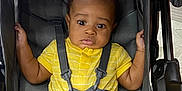 Jasiah is registered to the contest to win money with this photo: baby, child, stroller, yellow_outfit, harness, infant, seat, straps, curious, wide_eyes, indoor, padded, black, clothing, sitting, hands, legs, face, person, baby_girl