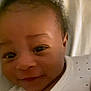 Jasiah is registered to the contest to win money with this photo: baby, infant, smiling, face, onesie, white_clothing, dots, curly_hair, lying_down, bed, blanket, video_call, phone_screen, car_interior, hand, person, sky, clouds, portrait, closeup