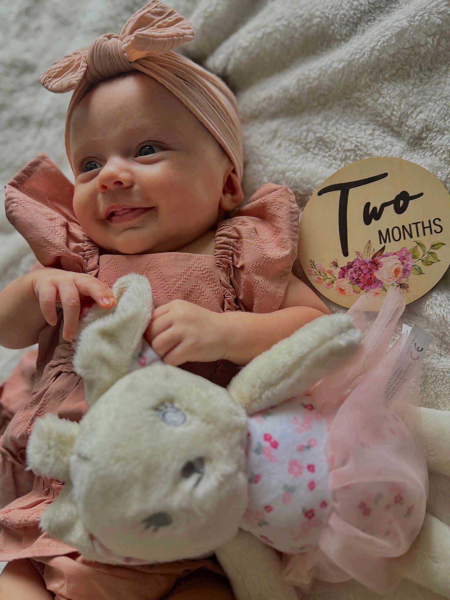 Vanni is registered to the contest to win money with this photo: baby, infant, smile, headband, plush_toy, bunny, blanket, milestone_sign, two_months, pink_clothing, soft_texture, cute, child, portrait, lying_down, hand, face, happy, indoors, cozy
