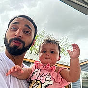 Arabella is registered to the contest to win money with this photo: man, baby, child, person, outdoor, cloudy_sky, house, building, facial_expression, beard, pink_clothing, minnie_mouse, cute, holding, portrait, casual, fun, family, human, smile
