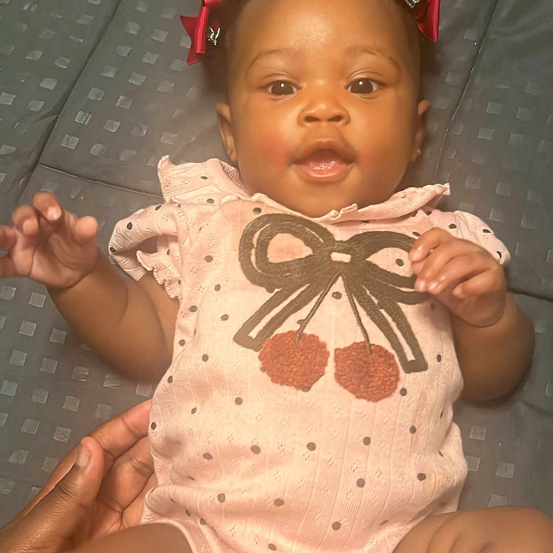 Nyairah joined the competition — help win amazing prizes! baby, infant, child, girl, pink_onesie, bows, hair_accessory, lying_down, hand, diaper, cute, smiling, happy, indoor, closeup, person, skin, expression, face, baby_girl