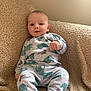 baby, infant, pajamas, elephant_pattern, blanket, beige, cozy, cute, child, portrait, indoor, smile, face, young, sitting, clothing, soft, comfort, relaxed, home