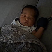 Azuré is registered to the contest to win money with this photo: baby, sleeping, blanket, couch, cozy, indoor, infant, mitten, face, head, clothing, star_pattern, comfort, rest, person, soft_texture, home, peaceful, relaxation, dark_hair