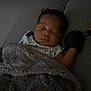 baby, sleeping, blanket, couch, cozy, indoor, infant, mitten, face, head, clothing, star_pattern, comfort, rest, person, soft_texture, home, peaceful, relaxation, dark_hair