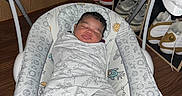 Mateo joined the competition — help win amazing prizes! newborn, baby, infant, sleeping, bouncer, blanket, swaddled, face, portrait, indoors, sneakers, shoe_rack, wood_floor, furniture, nursery, cozy, relaxed, patterned_fabric, feet, photograph