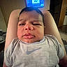 Mateo is registered to the contest to win money with this photo: baby, infant, child, portrait, face, serious_expression, indoors, sitting, held, arms, striped_shirt, clothing, nike_logo, television, screen, home, furniture, close_up, photography, funny_expression