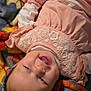 baby, child, smiling, pink_dress, embroidery, blanket, hand, lying_down, happy, indoor, close_up, infant, cute, soft_texture, colorful, person, face, portrait, toddler, warm