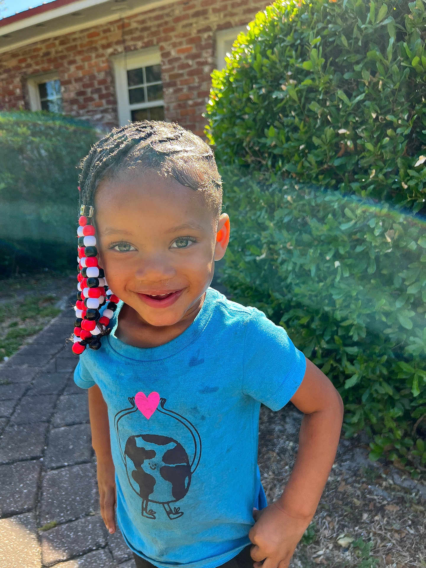 Kaylani joined the competition — help win amazing prizes! child, smiling, outdoor, sunlight, braids, beads, blue_tshirt, greenery, brick_house, happy, person, portrait, cute, kid, daylight, playful, young, standing, nature, casual