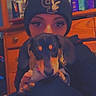 beanie, black_coat, bottles, cute, dog, drawers, dresser, eyelashes, hand, hat, holding, indoor, mirror, person, pet, portrait, puppy, selfie, shelf, wooden_furniture
