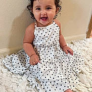 Azayla is registered to the contest to win money with this photo: baby, barefoot, bedroom, blanket, child, close_up, curly_hair, fashion, fluffy_blanket, hair_clip, happy, indoors, polka_dot_dress, portrait, sitting, smiling, toddler, wall, white_dress, wood_floor