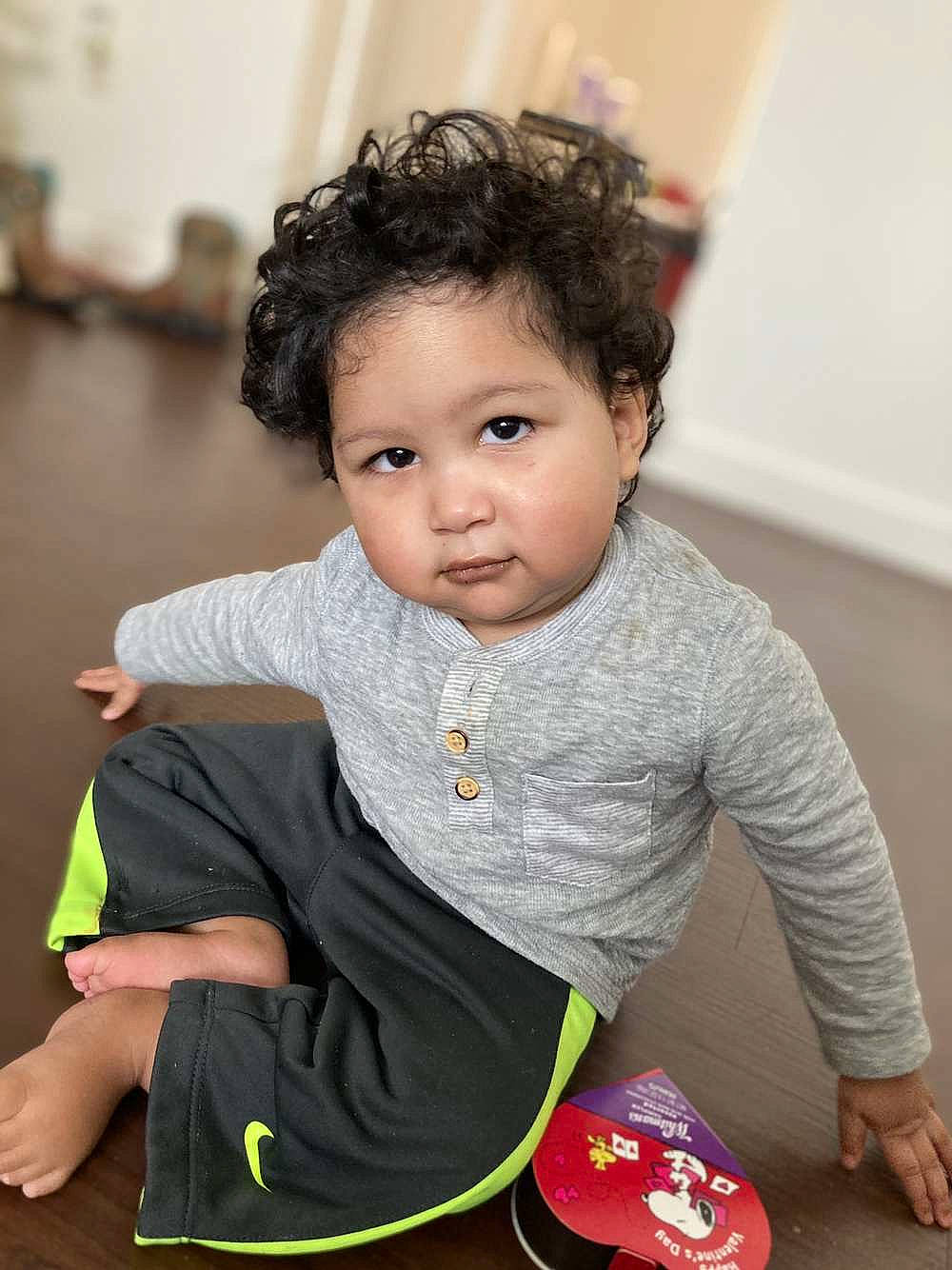 Omari is registered to the contest to win money with this photo: arm, baby, baby_toddler_clothing, cheek, child, eye, finger, flash_photography, floor, flooring, fun, happy, nose, person, portrait_photography, room, sitting, skin, sleeve, t_shirt