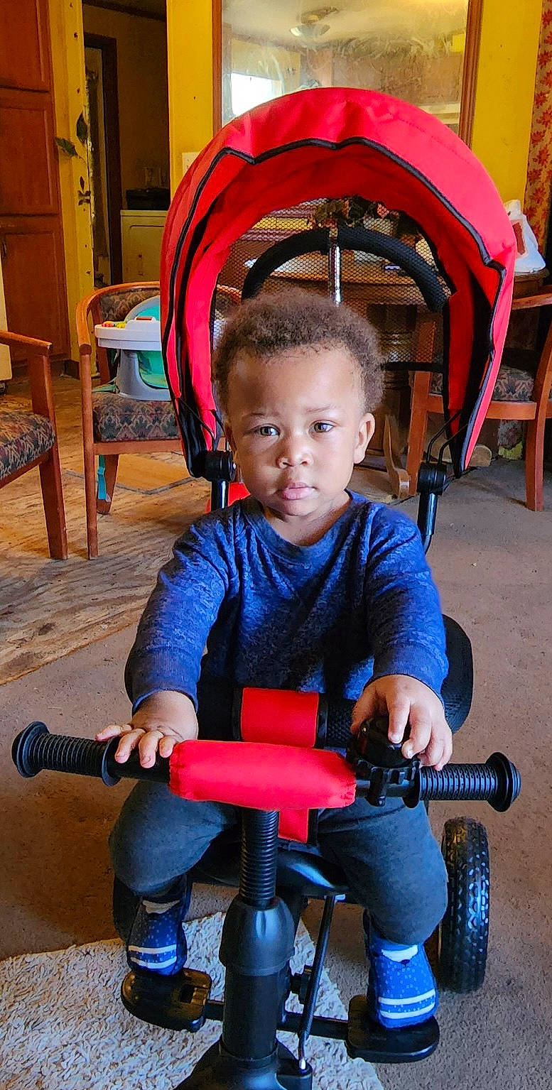 Dakarai is registered to the contest to win money with this photo: beauty, chair, child, city, electric_blue, event, fun, human_leg, knee, leisure, person, play, product, recreation, riding_toy, sitting, tire, toddler, vacation, wood