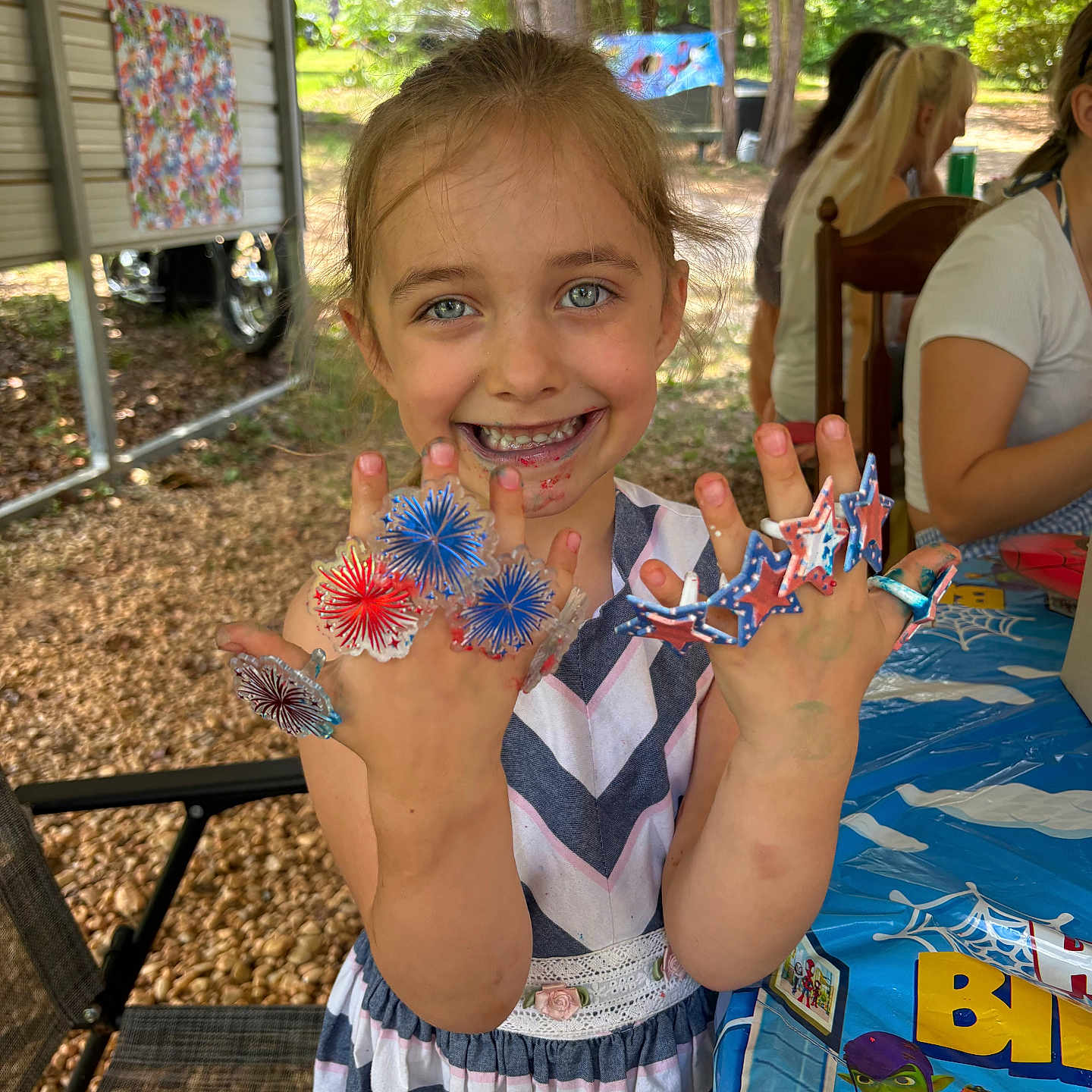 Naomi is registered to the contest to win money with this photo: child, girl, smile, face, hands, rings, colorful, birthday, table, tablecloth, outdoor, party, decoration, chair, people, hair, clothing, nature, celebration, happy