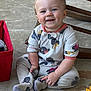 Noah joined the competition — help win amazing prizes! baby, child, smile, onesie, sitting, concrete_floor, rocking_chair, red_bin, happy, face, person, footwear, patterned_clothing, cute, infant, indoors, toes, hand, playful, blue_eyes