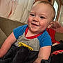 Noah is registered to the contest to win money with this photo: toddler, child, smile, blanket, couch, indoors, curtain, window, face, blue_shirt, happy, skin, person, sitting, cozy, home, red_detail, soft_light, hair, cheeks