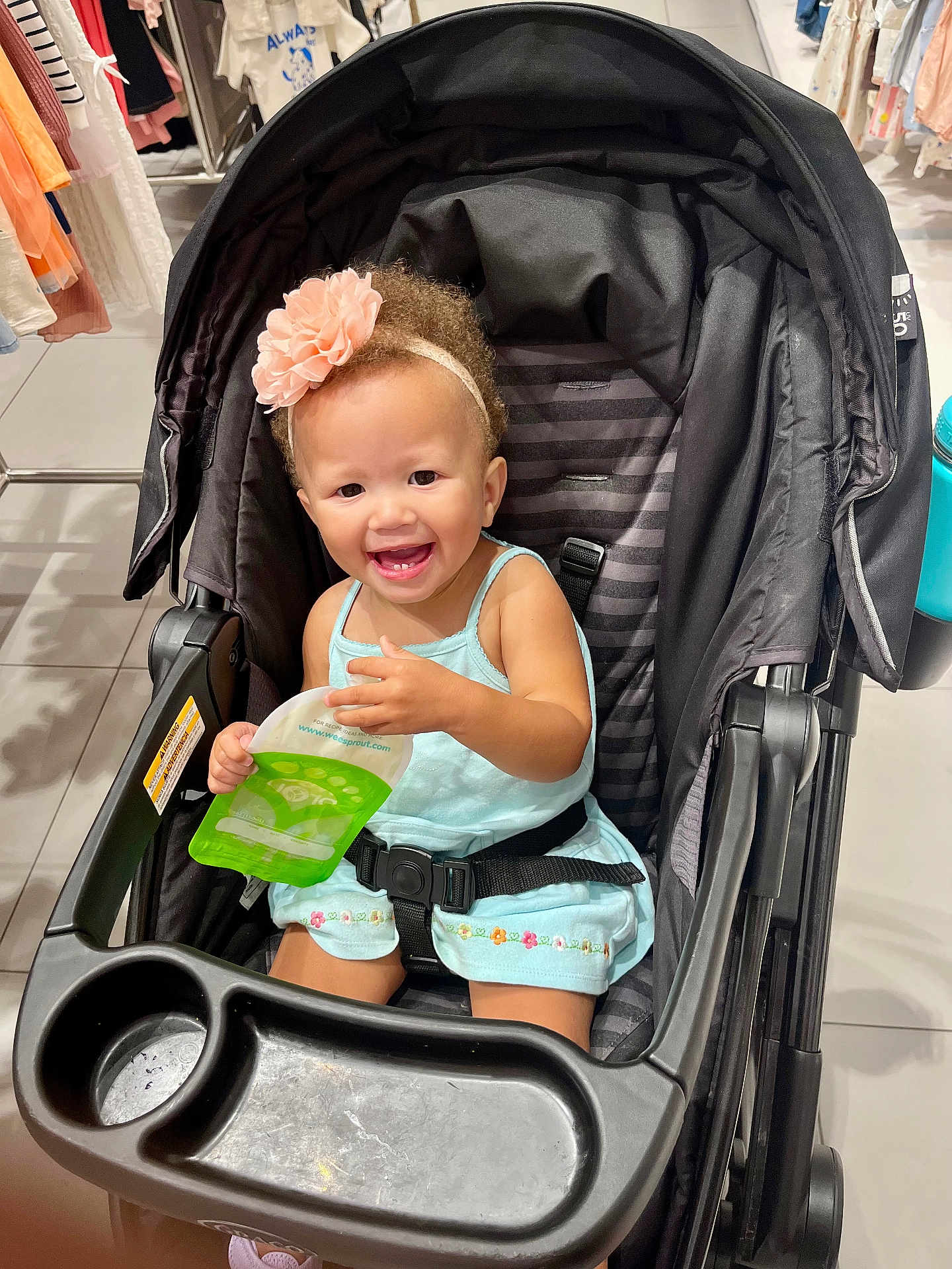 Aniyah joined the competition — help win amazing prizes! toddler, smiling, flower_headband, stroller, child, blue_dress, indoor, shopping, clothing_rack, happy, seat_belt, toy_or_snack_pouch, retail, floor_tile, person, baby, cute, hair, cart, store