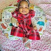 Camila is registered to the contest to win money with this photo: animal_print, baby, blanket, bow, child, cushion, cute, feet, happy, headband, indoors, infant, patterned_background, pink_flowers, plaid, portrait, red_dress, sitting, smiling, white_socks