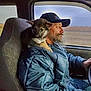 man, puppy, dog, beard, cap, jacket, truck_interior, seat, window, steering_wheel, road, countryside, driving, pet_on_shoulder, companion, portrait, cozy, travel, adorable, candid
