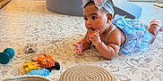 Myah is registered to the contest to win money with this photo: baby, child, toddler, toy, wooden_toy, headband, blue_dress, carpet, playroom, basket, teething_ring, animal_blocks, slide, floor, indoor, cute, chewing, patterned_carpet, colorful, natural_light
