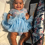 Myah is registered to the contest to win money with this photo: baby, child, smiling, blue_dress, headband, cushion, fabric, indoor, cute, infant, happy, person, skin, legs, arms, sitting, portrait, clothing, comfort, baby_girl