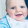 baby, being_held, bib, blue_clothing, cheeks, close_up, ear, eyes, face, hair, happy, indoor, infant, mouth, person, planet_pattern, portrait, skin, smiling, wall