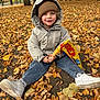 Tyler participe au concours pour gagner de l'argent avec cette photo : autumn, casual_clothing, child, daylight, fall, flag, ground, happy, hat, jacket, leaves, nature, outdoor, park, seasonal, sitting, smiling, trees, white_shoes, young_child