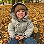 autumn, casual_clothing, child, cool_weather, daylight, fall_leaves, happy, hat, jacket, leaves, nature, outdoor, park, person, portrait, seasonal, sitting, smiling, trees, young_child