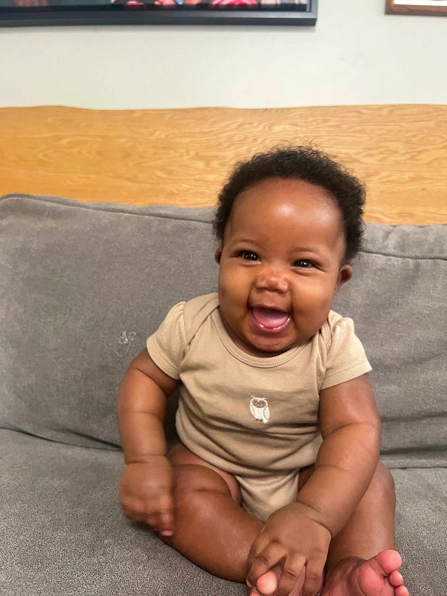 Eternal is registered to the contest to win money with this photo: baby, smiling, infant, onesie, couch, gray_couch, happy, child, cute, sitting, indoor, portrait, young_child, skin, face, hand, foot, furniture, wood, cozy