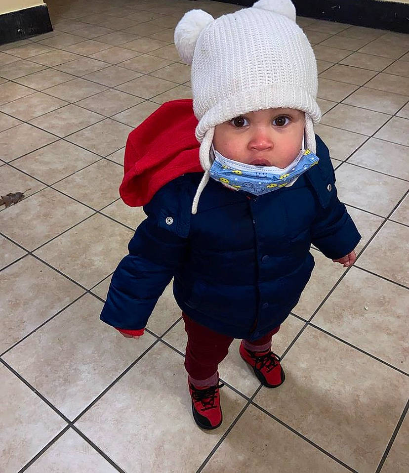 Jared is registered to the contest to win money with this photo: baby, baby_toddler_clothing, beanie, cap, carmine, child, electric_blue, floor, flooring, fur, headgear, headwear, knit_cap, outerwear, pattern, person, road_surface, sitting, sleeve, toddler