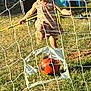 active, blond_hair, child, child_playing, dress, fence, field, game, goal_net, grass, happy, kick, net, outdoor, playground, recreation, soccer_ball, sport, sunlight, toy