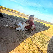 Annabelle is registered to the contest to win money with this photo: child, blonde_hair, cat, outdoor, sunny, dirt, grass, boots, crouching, petting, happy, smiling, sky, animal, nature, casual_clothing, playful, daylight, cute, young