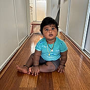 Ram joined the competition — help win amazing prizes! baby, child, indoor, floor, wooden_floor, hallway, blue_shirt, fish_print, necklace, sitting, curious, wide_eyes, person, young_child, casual_clothing, skin, hair, toe, hand, home