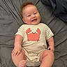 baby, infant, smiling, happy, onesie, striped_clothing, crab_graphic, lying_down, blanket, soft_fabric, cute, toddler, child, skin, face, expression, hair, indoors, person, playful