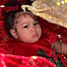 baby, child, face, red_dress, curly_hair, bow, holiday, festive, glitter, sparkle, fabric, portrait, closeup, indoors, cute, serious_expression, celebration, infant, person, decorations