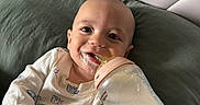 Orion is registered to the contest to win money with this photo: baby, bottle, milk, cushion, headboard, smile, face, infant, clothing, white, green, hand, lying_down, happy, cute, indoors, portrait, feeding, soft, comfort
